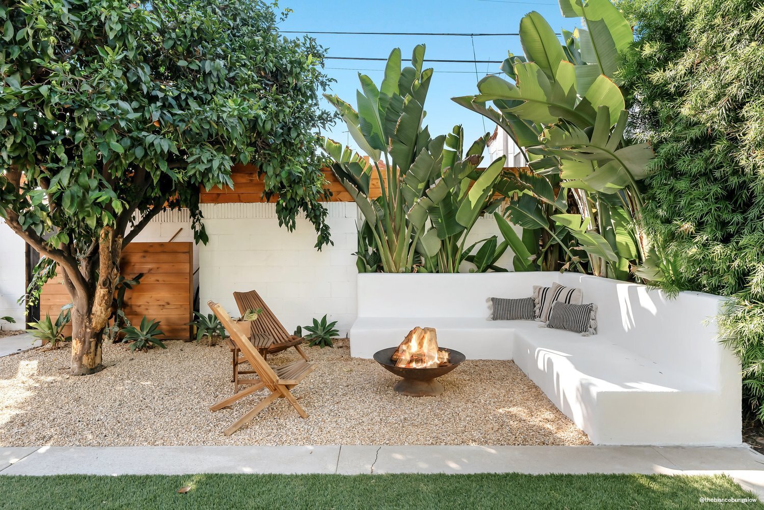 pea gravel patio with built-in bench seating, lounge chairs, and metal fire pit with tropical plantings in background