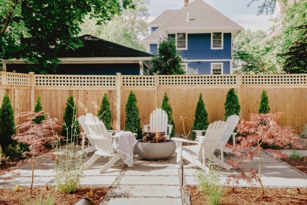 Fire pit and white Adirondack chairs on top of pavers with lush plantings
