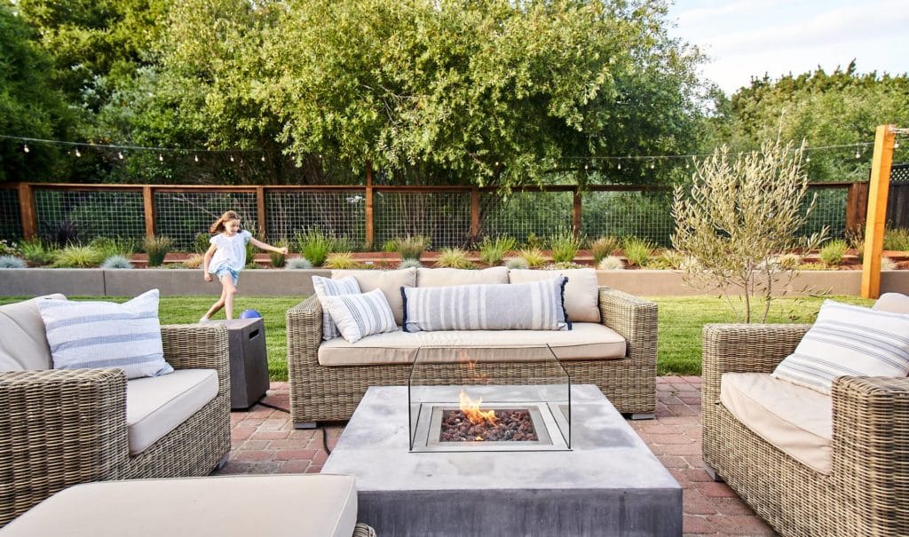 Young girl plays with ball in newly renovated backyard with outdoor fire pit area with seating