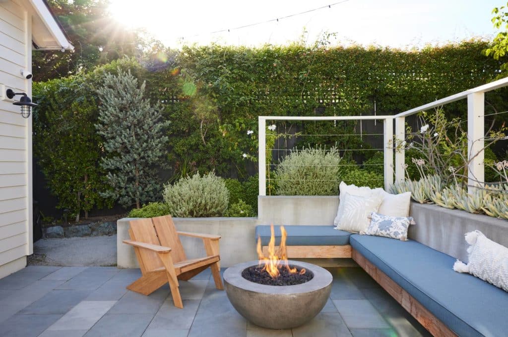A built-in outdoor sectional with planting bed behind surrounding round fire pit on paved patio