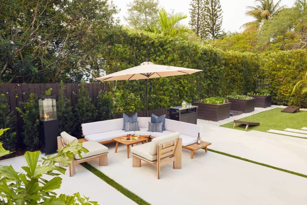 Tropical backyard patio with furniture, garden boxes, and cornhole game