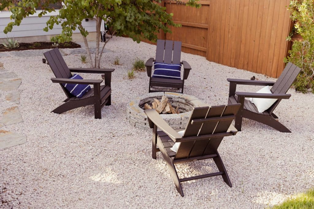 Simple round block fire pit on gravel with 4 black Adirondack chairs