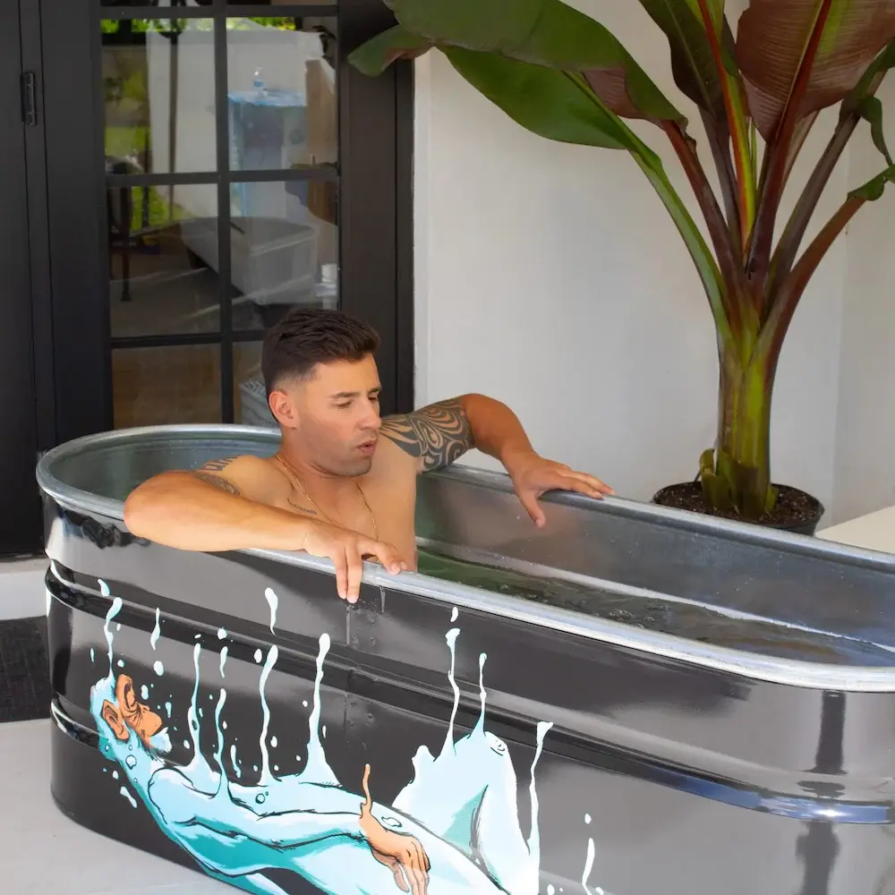 Man lowering into cold plunge tub with custom artwork painted on the side