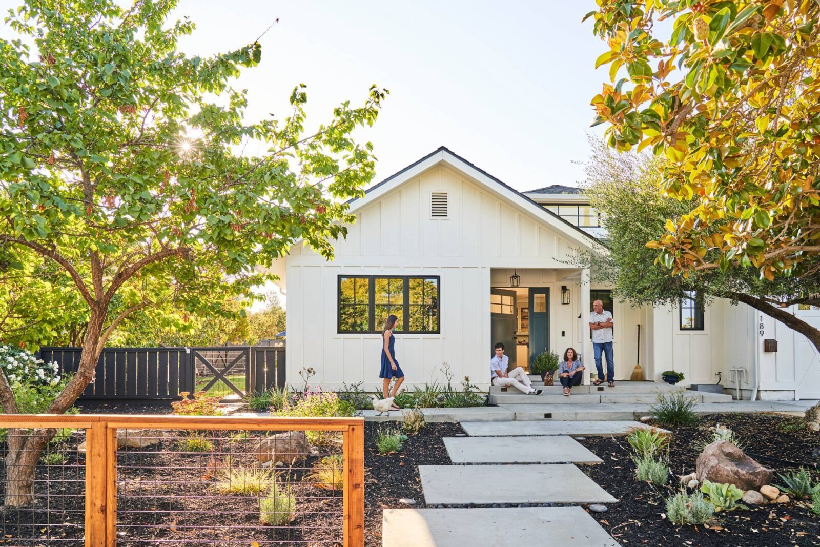 A family on the front porch of a modern farmhouse style home with fresh hardscaping and drought tolerant planting.